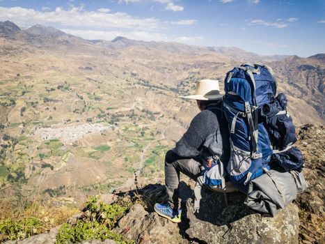Traveler man with hat and backpack sitting on a rock watching the landscape, Travel lifestyle