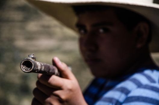 Close up face of boy with hat pointing with a rifle