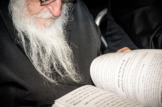 Senior man reading book at work desk with eyeglasses on foreground
