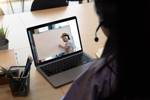 Asian young girl student learning virtual internet online class from school teacher by remote meeting due to covid pandemic. Female teaching by using headphone and whiteboard.