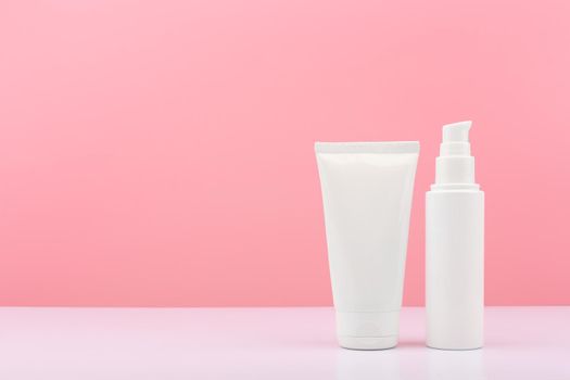Two white cosmetic tubes on white table against pink background with copy space. Concept of skin care and beauty