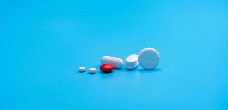 Group of round and oval white tablets pills, red sugar-coated tablets pills on blue background. Pharmacy shop and pharmacy department banner. Pharmaceutical industry. Health care. Drugs in daily life.