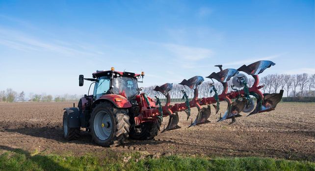 tractor with plough on field early spring in the netherlands on the island of goeree en overflakkee under blue sky