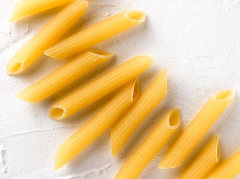 Raw pasta as food background. Italian Penne Rigate Macaroni Pasta on textured white background. Dried pasta selection close up. Top view or flat lay with copy space