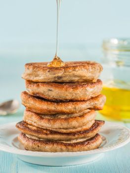 Stack of small pancakes with banana and chia seeds in honey on light blue background. Honey pouring over stack of mini pancakes with chia or poppy seeds.