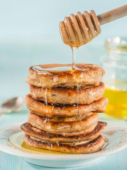 Stack of small pancakes with banana and chia seeds in honey on light blue background. Honey pouring over stack of mini pancakes with chia or poppy seeds.