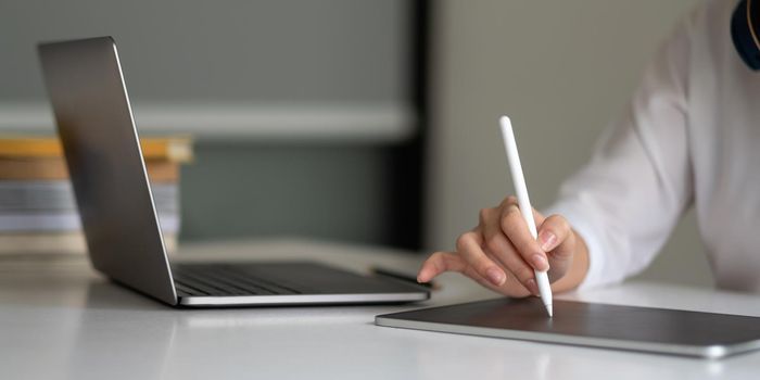 Close up hand of woman with stylus pen writing on digital notepad, touching on digital tablet screen working on laptop computer in office. Web designer working his project