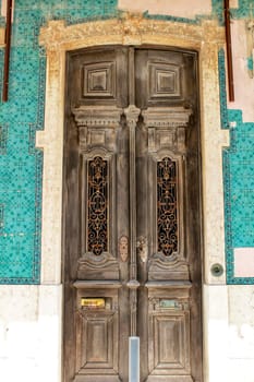 Old wooden door with tiled facade in Lisbon. Wrought metal details on the door.