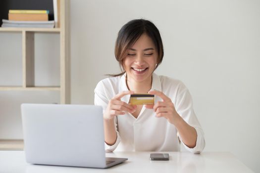 Happy asian woman using her credit card for online shopping at home office