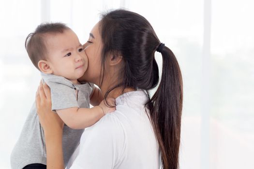 Young asian mother holding little baby girl together in the bedroom at home, mom carry child and care, woman and kid with carefree, toddler and parent, emotion and expression, family concept.