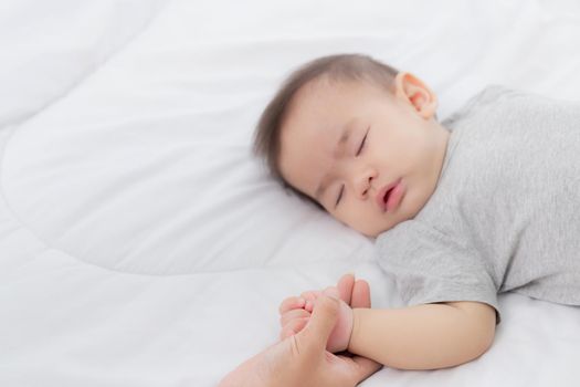 Young asian mother touch hand of little baby girl with tender on bed in the bedroom, mom love newborn and care, woman with expression with child together, parent and daughter, family concept.