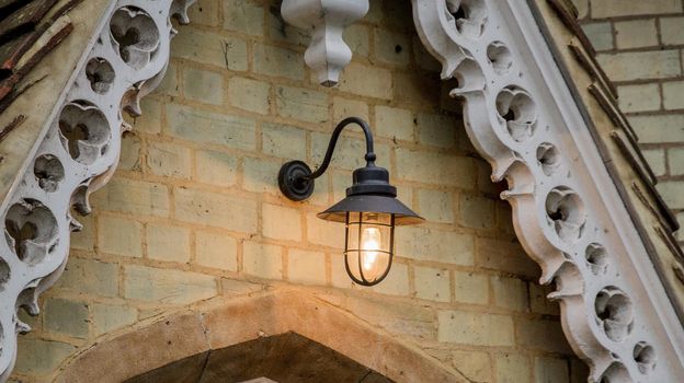 Detail of a black metal lamp with a ligthed bulb hanging on a yellow brick wall