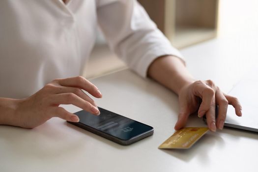 Close up woman using smart phone and laptop computer and credit card for shopping online at home