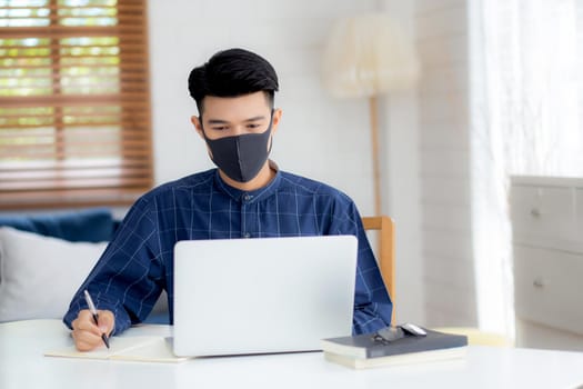 Young asian business man in face mask for protect covid-19 and work on laptop computer and writing notebook, businessman quarantine work from home, new normal, social distancing and stay home.