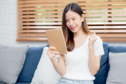 Young attractive asian woman resting using browsing tablet computer on sofa at home, happy girl sitting on couch relax reading digital gadget with excited at house, communication and lifestyle concept.