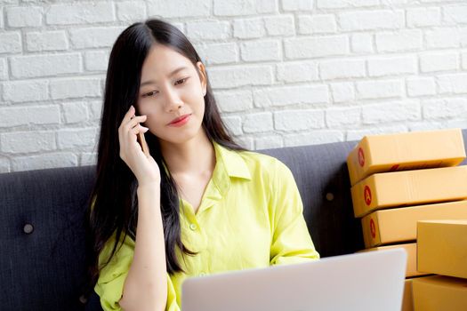 Young asian woman is entrepreneur talking with customer and using laptop computer while order purchase online at home, logistic and delivery, online shopping, female is seller of business SME.