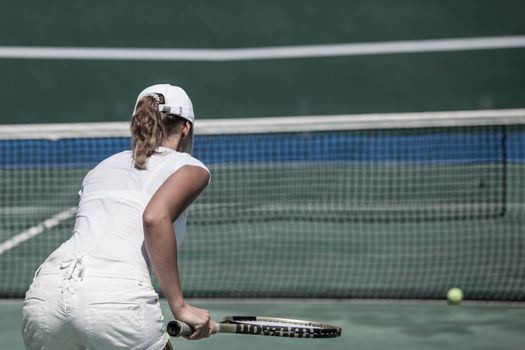 Back view of woman in white tennis uniform playing tennis on court