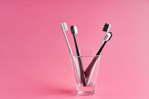 Fashionable toothbrush with soft bristles. Popular toothbrushes. Hygiene trends. Kit of toothbrushes in glass on pink background.