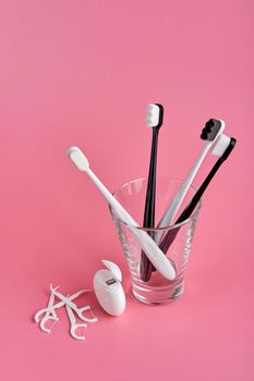 Fashionable toothbrush with soft bristles. Popular toothbrushes. Hygiene trends. Oral hygiene kit. Toothbrushes in glass, floss thread and toothpicks on a pink background.