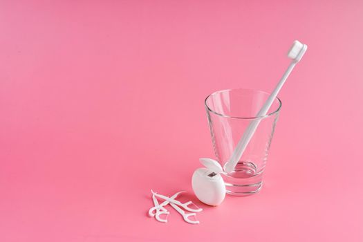 Fashionable toothbrush with soft bristles. Popular toothbrushes. Hygiene trends. Oral hygiene kit. Toothbrushes in glass, floss thread and toothpicks on a pink background.