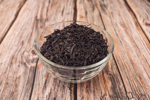 Dry leaves of long tea lie in a glass bowl on a wooden table close-up