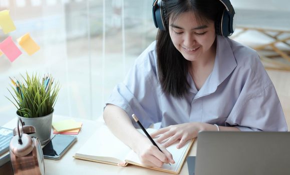 Focused young girl wearing modern headphones looking at laptop monitor, listening to educational lecture webinar, writing notes. Motivated millennial woman studying remotely in online university.
