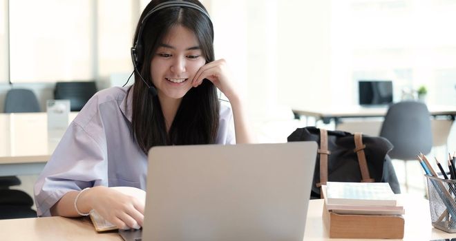 Young woman having online training, using laptop and wireless headset
