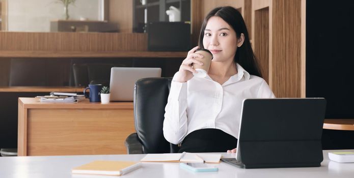 Portrait of young businesswoman using laptop screen while sitting at office desk in modern office

