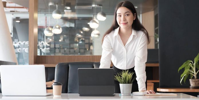 Confident businesswoman standing at her office desk and smiling to camera.
