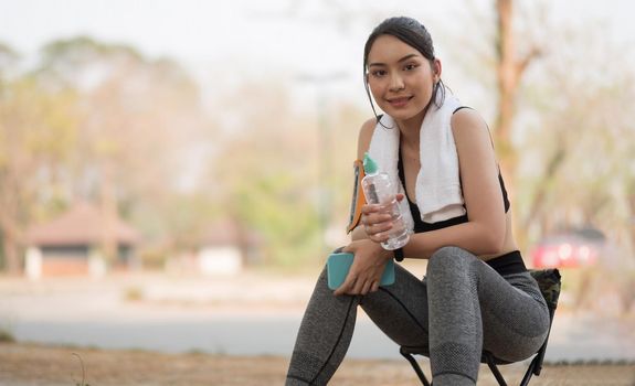 Young athletic woman holding water from a bottle after running in the park.