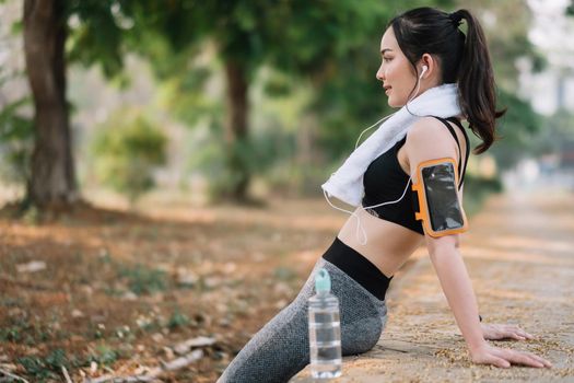 Athletic asian woman resting after a hard training in the mountains at sunset. Sport tight clothes.