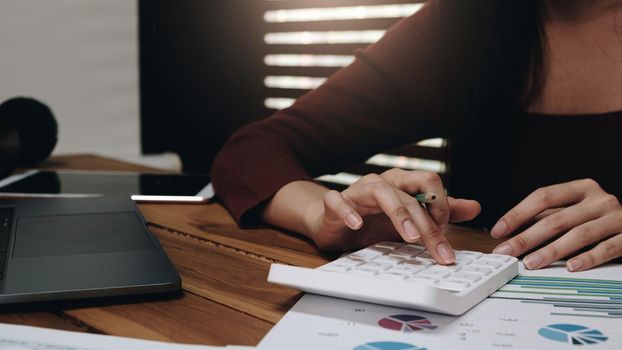 Close up Business woman using calculator and laptop for do math finance on wooden desk in office and business working background, tax, accounting, statistics and analytic research concept
