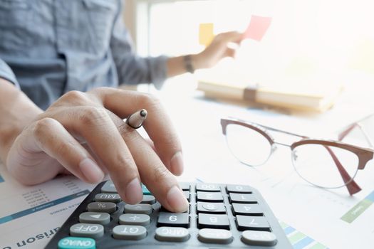 businessman or accountant hand working on calculator to calculate financial data report, accountancy document and laptop computer at office