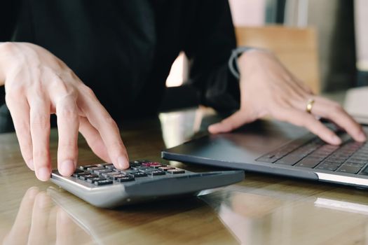 Close up Businesswoman using calculator and laptop for do math finance on wooden desk in office and business working background, tax, accounting, statistics and analytic research concept
