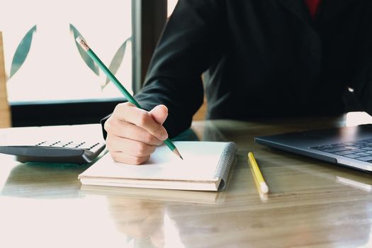 Close up of woman or accountant hand holding pen working on laptop computer for calculate business data, accountancy document and calculator at office, business concept
