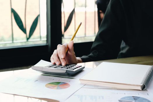 Close up Businesswoman using calculator and laptop for do math finance on wooden desk in office and business working background, tax, accounting, statistics and analytic research concept
