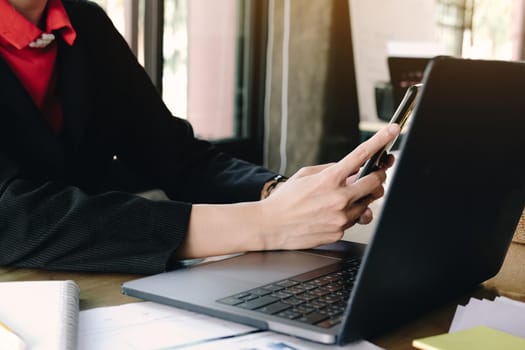 Close-up  businesswoman working in office interior on pc holding smartphone.