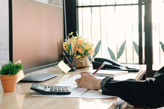 Close up of businessman or accountant hand holding pencil working on calculator to calculate financial data report, accountancy document and laptop computer at office, business concept
