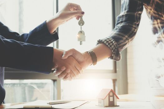 Estate agent shaking hands with his customer after contract signature, Contract document and house model on wooden desk
