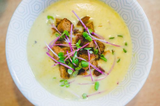 Close up of fresh broccoli soup with crunchy croutons and radish sprouts in white ceramic bowl
