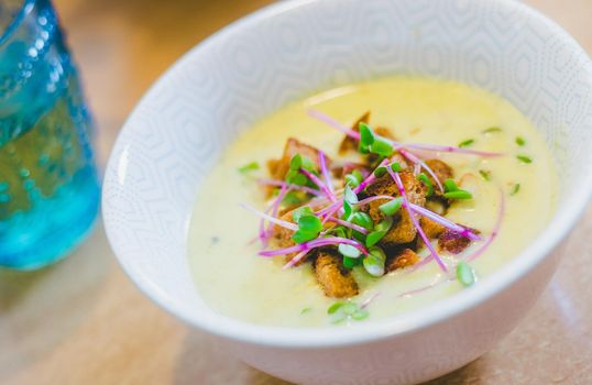 Close up of fresh broccoli soup with crunchy croutons and radish sprouts in white ceramic bowl