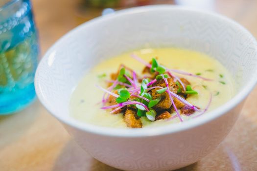 Close up of fresh broccoli soup with crunchy croutons and radish sprouts in white ceramic bowl