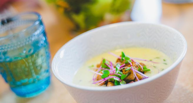 Close up of fresh broccoli soup with crunchy croutons and radish sprouts in white ceramic bowl