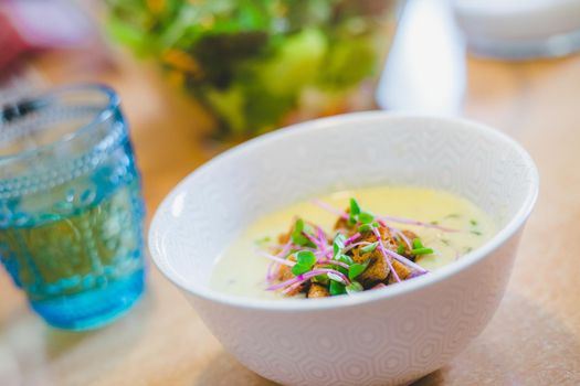 Close up of fresh broccoli soup with crunchy croutons and radish sprouts in white ceramic bowl