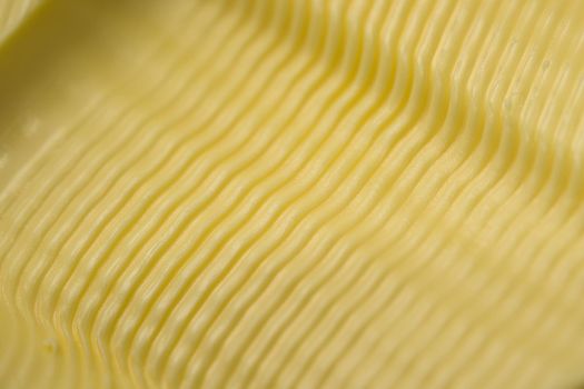 Wavy ripple pattern in butter created by a serrated butter knife. Full frame abstract food texture background, taken as a super macro close up.