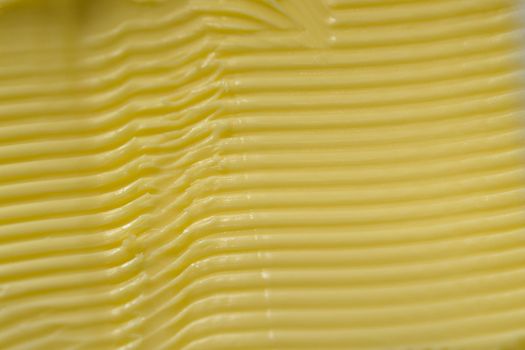 Super macro image of spreadable yellow margarine, after having a kitchen knife run through it to create a texture of horizontal grooves and ridges