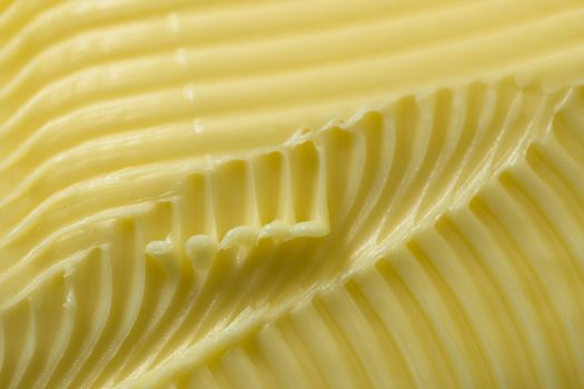 Close up of yellow butter. Full frame textured background, with a super macro perspective. Serrated butter knife used to create the abstract patterns