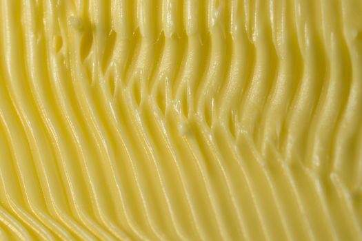 Food themed background of margarine. Shaped into detailed yellow grooves by a serrated kitchen knife used to spread it on bread. Full frame texture.