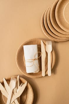 Reusable, disposable and recycling concept. Brown craft disposable bag and tableware cup, plate, and wooden fork, knife on brown background flat lay top view