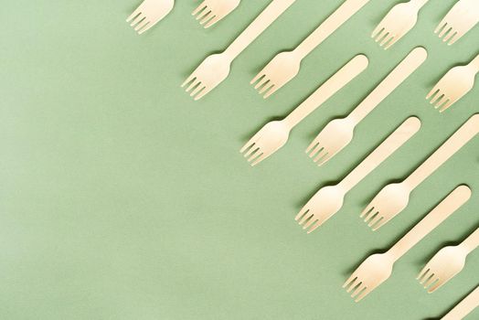 Reusable, disposable and recycling concept. Disposable wooden forks top view on green background with copy space